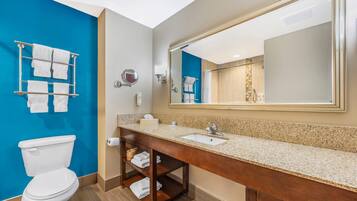 A modern bathroom with a blue accent wall, a large mirror, a wooden vanity, and a white toilet.