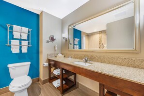 Une salle de bain moderne avec un mur d’accent bleu, un grand miroir, un meuble-lavabo en bois et des toilettes blanches.