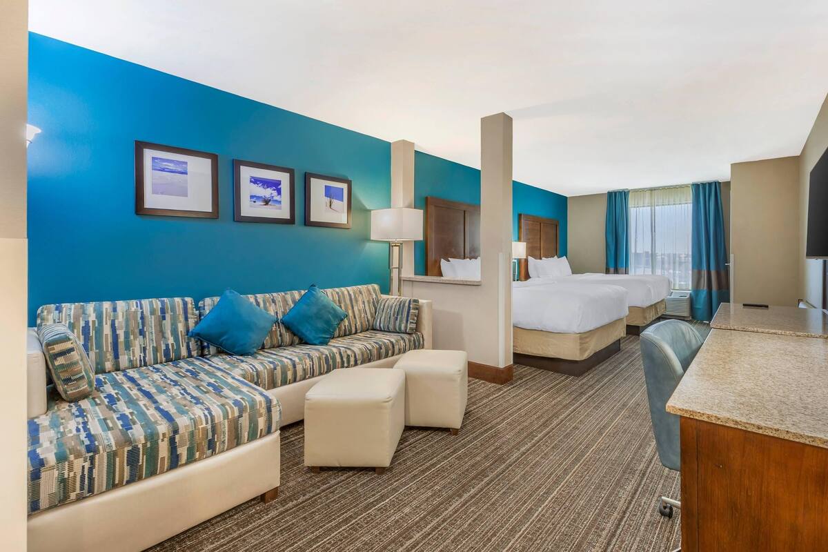 A hotel room with a blue accent wall, a sofa, a bed, a desk, and a mirror.