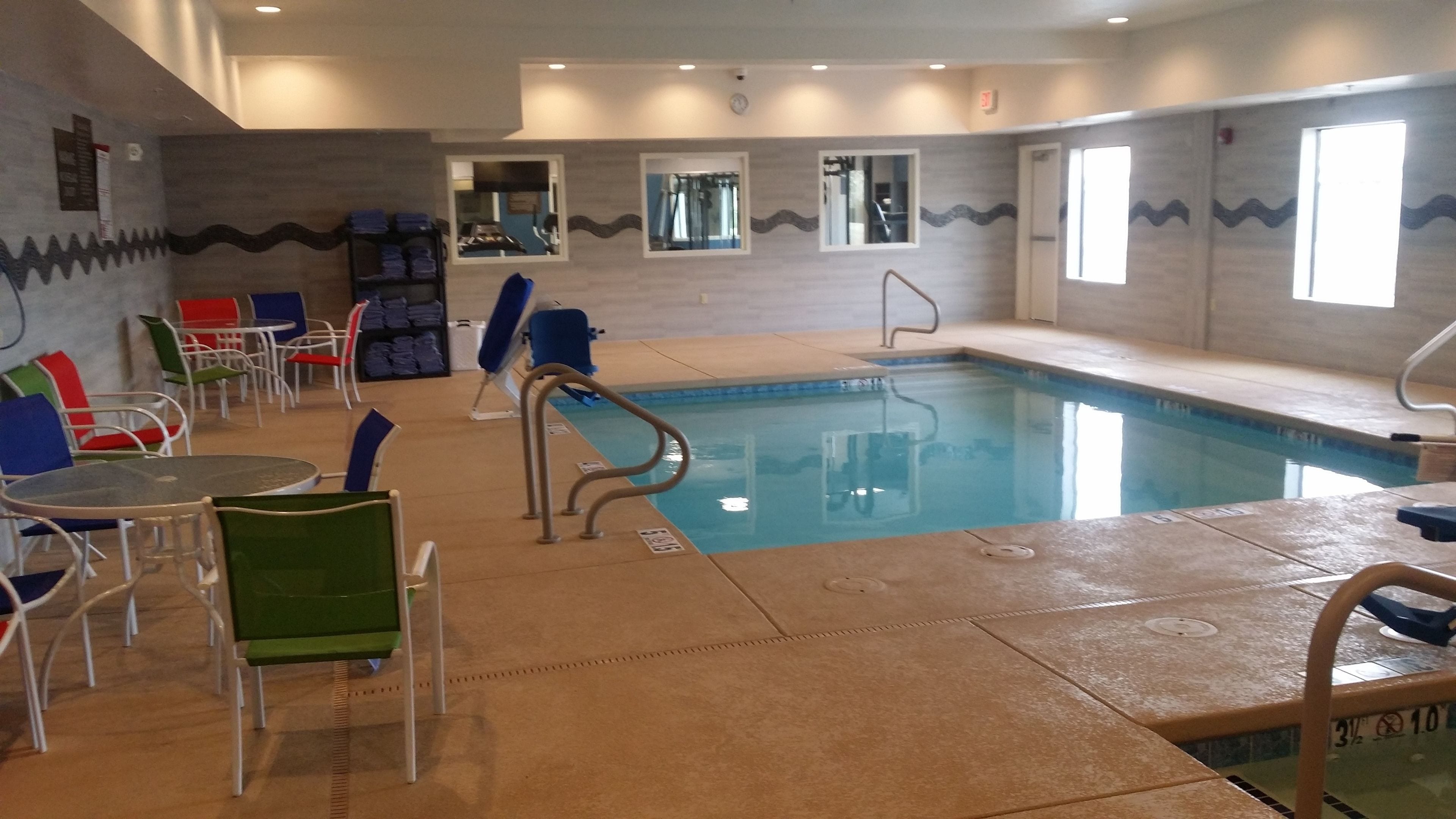 An indoor swimming pool with a tiled floor, surrounded by chairs and tables.