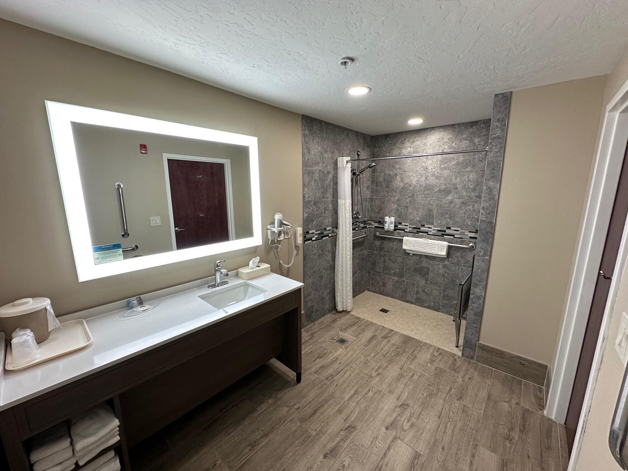 A modern bathroom with a large mirror, two sinks, a shower, and a towel rack.