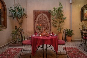 A dining area with a table set for two, surrounded by potted plants and a decorative wall panel. - Riad Dar Attika (Marrakech)