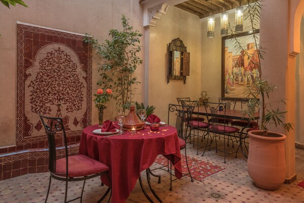 A dining area with a round table set for two, surrounded by chairs. - Riad Dar Attika (Marrakech)