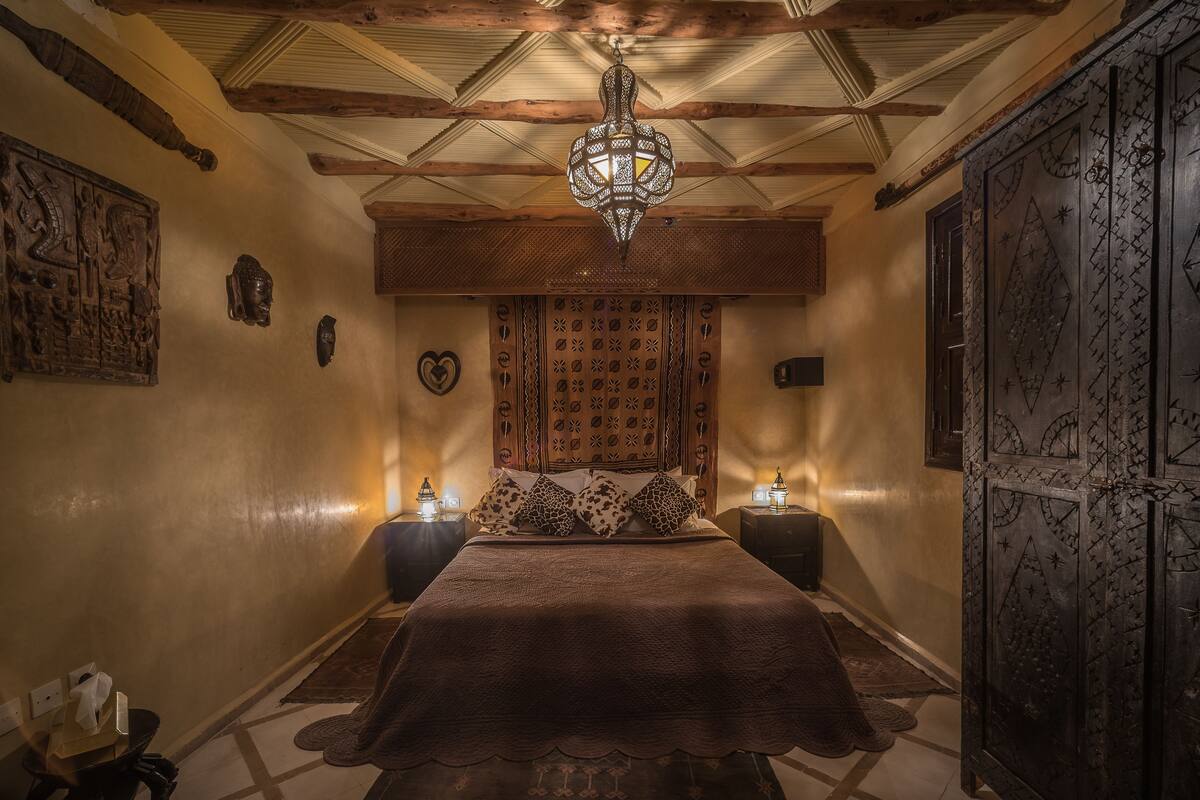 A room with a bed, wooden headboard, patterned wall decor, and a decorative door.