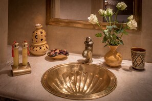 A bathroom sink with a decorative bowl, a mirror, a vase with white roses, and a decorative jug. - Riad Dar Attika (Marrakech)