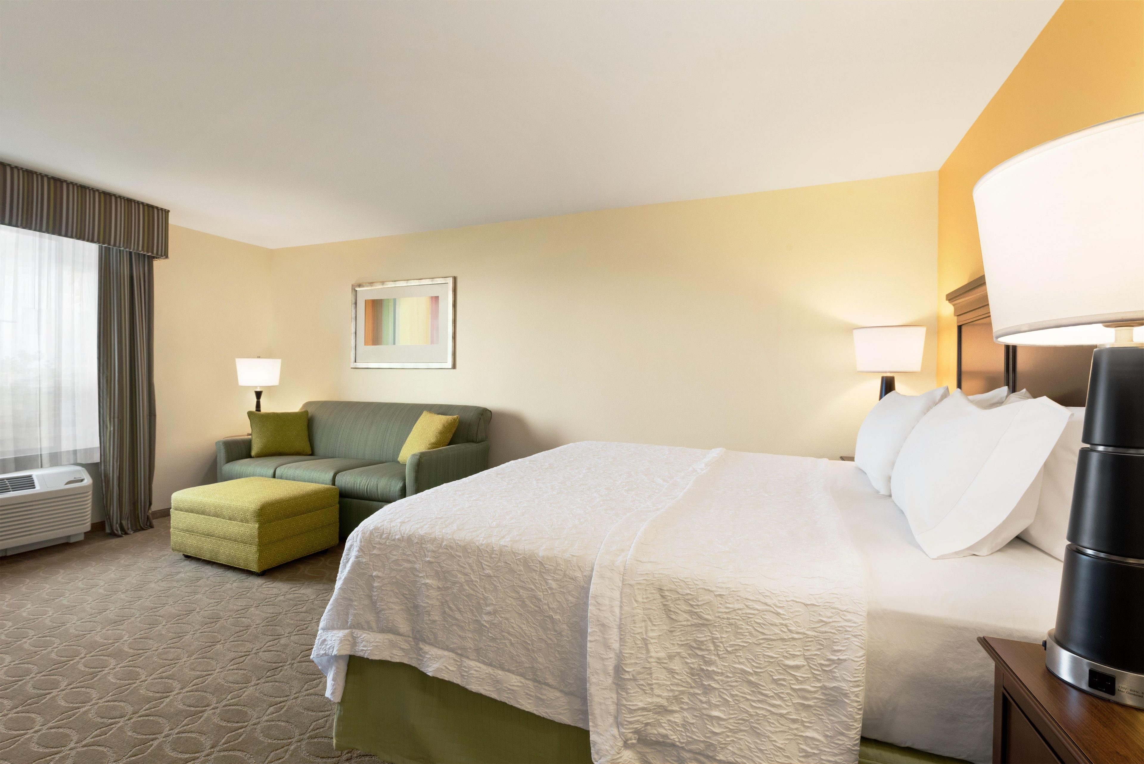 A hotel room with a bed, a sofa, a small table, a lamp, and a picture on the wall.