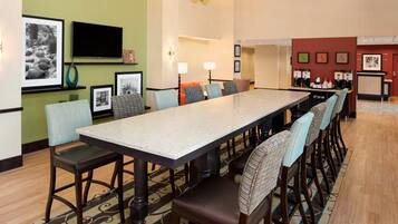 A hotel dining area with a long table, chairs, and a coffee station.
