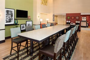 Un espace de restauration d'hôtel avec une longue table, des chaises et un coin café.
