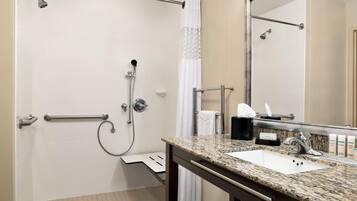 A bathroom with a shower, a sink, a mirror, and a towel rack.