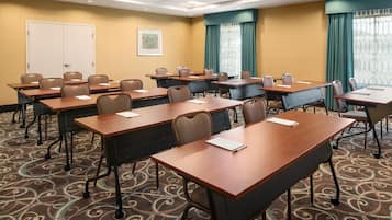 A conference room with multiple tables and chairs, carpeted floor, and a door in the background.