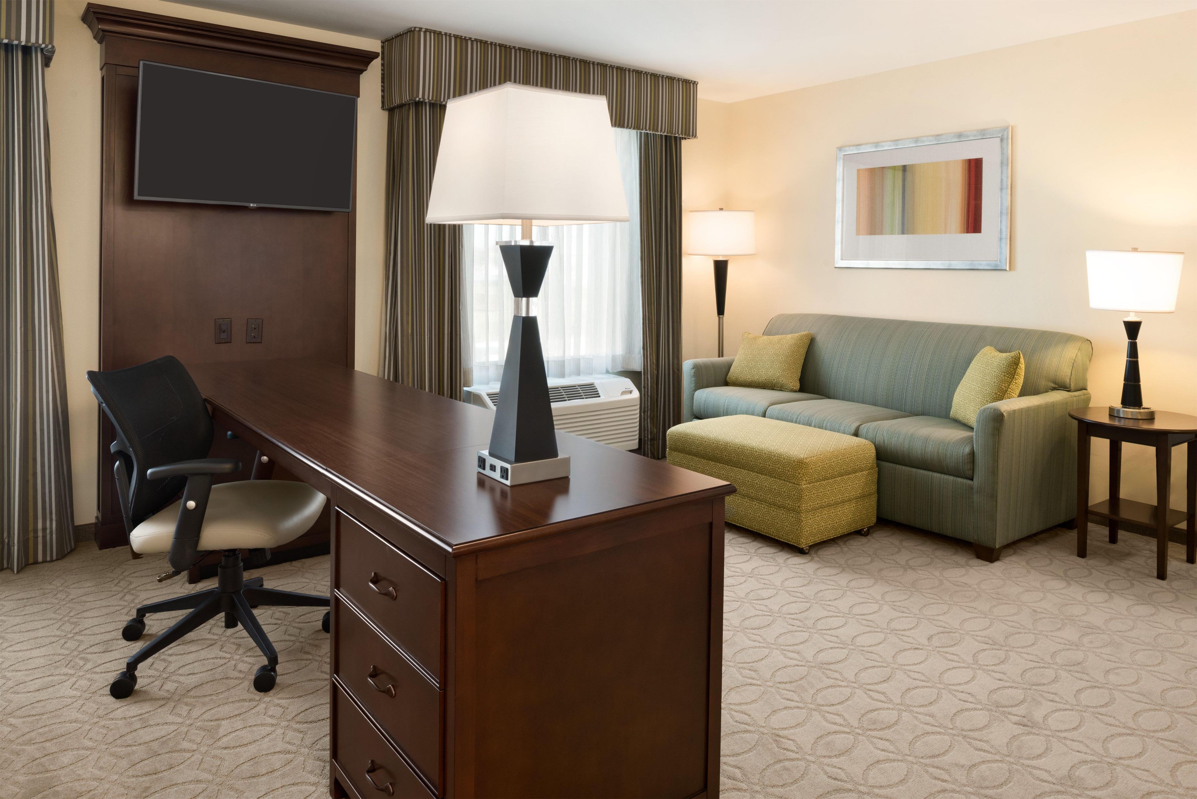 A hotel room with a desk, office chair, sofa, and two bedside lamps.