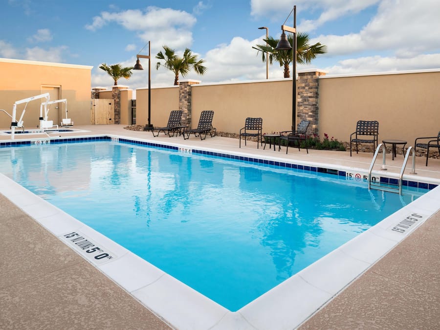A rectangular swimming pool with a clear blue water surface, surrounded by lounge chairs and a stone wall.