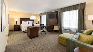 Quarto de hotel com cama, escrivaninha, cadeira e sofá.