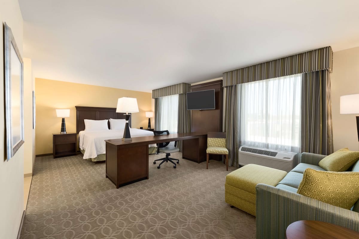 A hotel room with a bed, desk, chair, and sofa.
