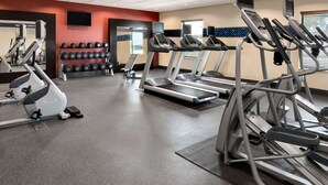 Uma academia com esteiras, halteres e equipamentos de exercícios cardiovasculares.