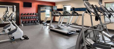 Un gimnasio con cintas de correr, mancuernas y equipo cardiovascular.