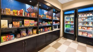 Uma área de exposição de lanches e bebidas, com prateleiras cheias de diversos snacks e uma seção refrigerada para bebidas.