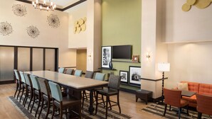 Uma sala de conferências com uma mesa comprida, cadeiras, um sofá e uma TV.