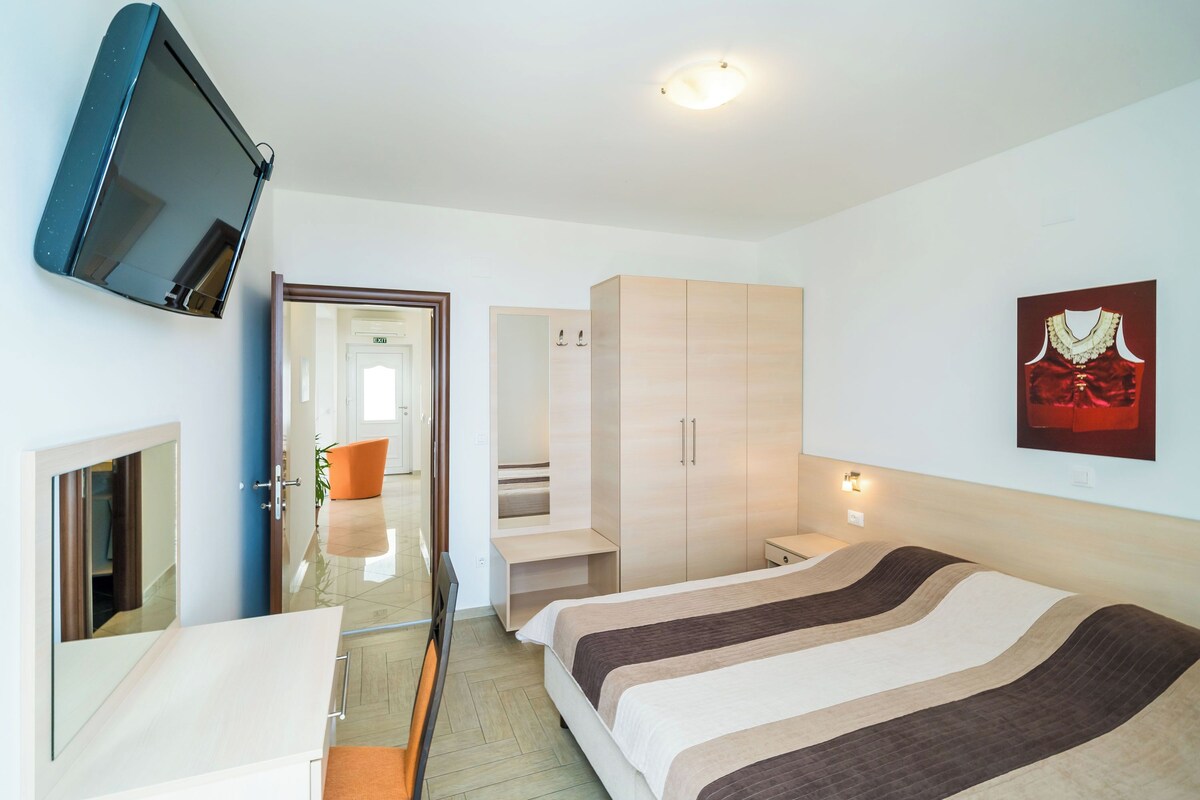 A hotel room with a bed, a TV mounted on the wall, a wardrobe, and a framed picture on the wall.