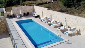 A swimming pool with lounge chairs and umbrellas, surrounded by stone walls and greenery.