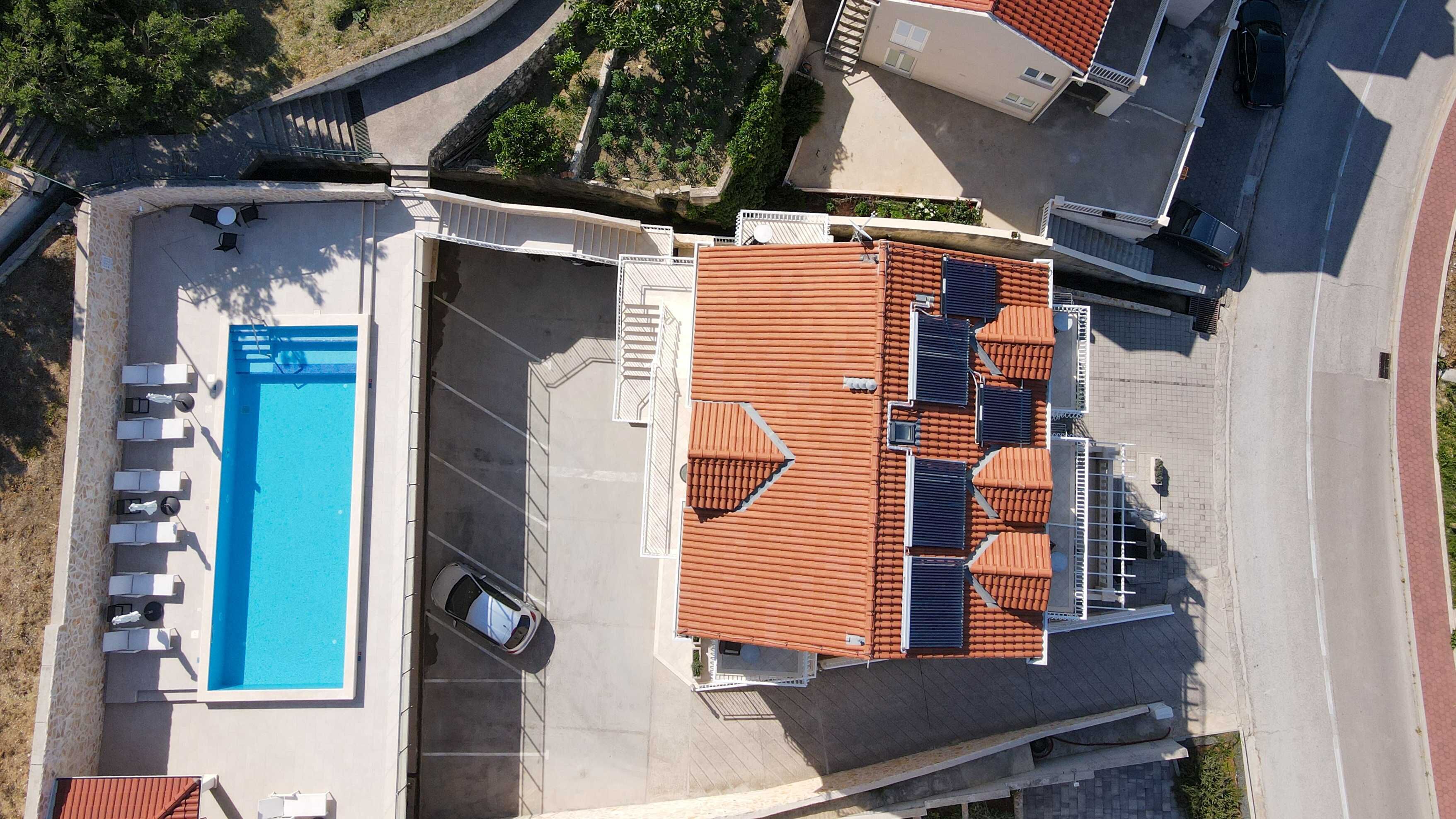 An aerial view of a residential property with a swimming pool, outdoor seating, and a tiled roof.