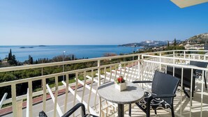 A balcony with a table and chairs, overlooking a coastal view with a clear sky.