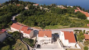 An aerial view of a coastal property with a swimming pool, terraced houses, and a road curving through the landscape.