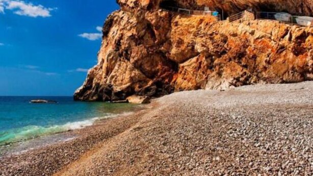 A rocky cliff with a building on top, overlooking a pebble beach and the sea.