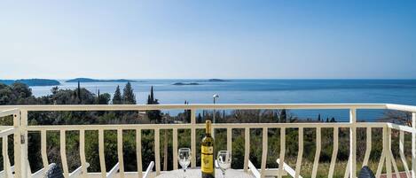 Ein Balkon mit Tisch und Stühlen, der auf ein Gewässer und entferntes Land blickt.