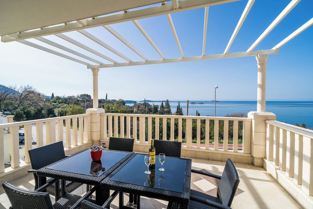 A terrace with a table and chairs, a bottle of wine, and a view of the sea.