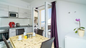 A modern kitchen with a microwave, coffee maker, and kettle. There is a dining table with chairs and a potted plant.