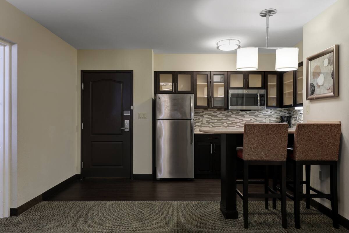 A compact kitchen with dark wooden cabinets, stainless steel appliances, and a tiled backsplash.
