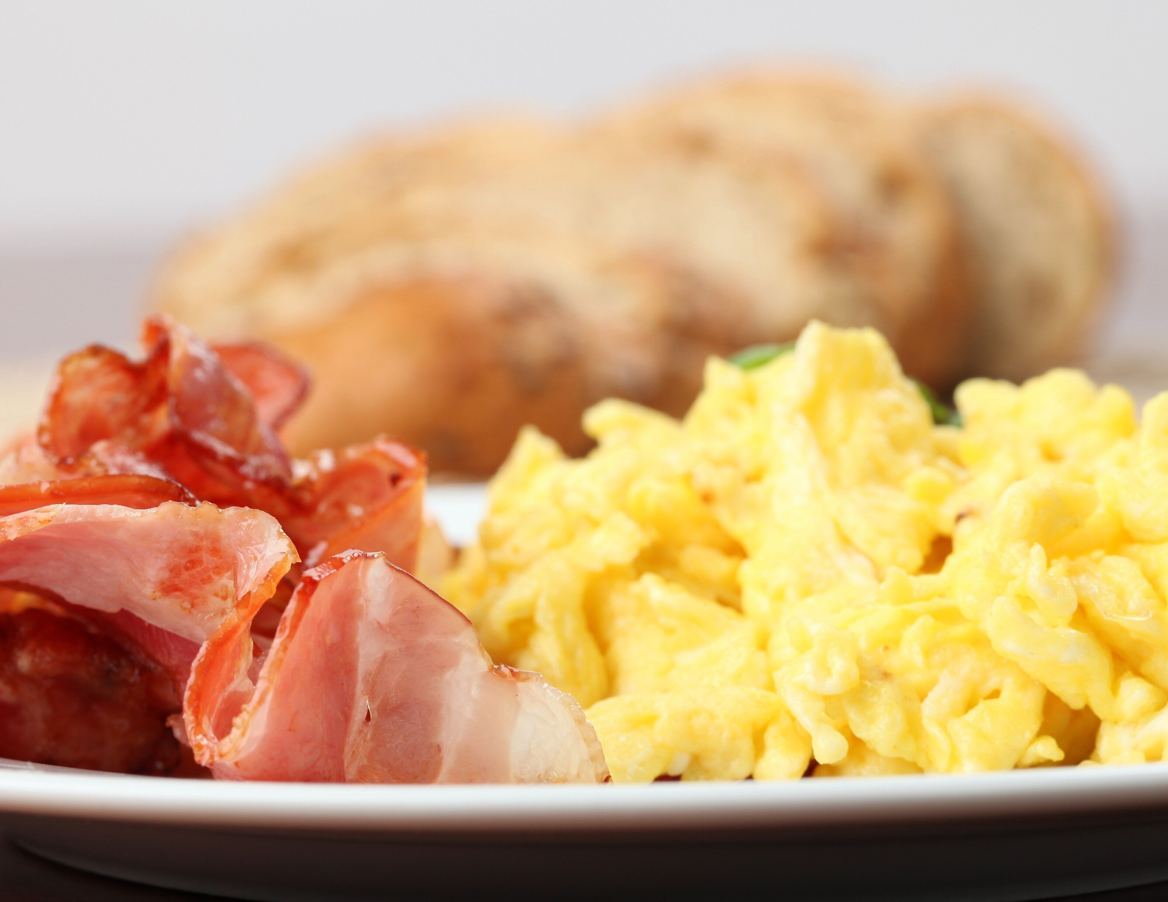 A plate with scrambled eggs, bacon, and a piece of toast.