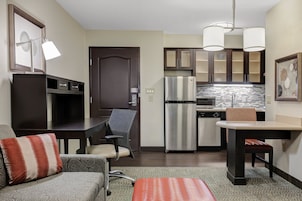 Una cocina compacta con refrigerador, microondas y una pequeña zona de comedor con mesa y sillas.
