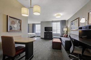 Una habitación de hotel con cama, escritorio, sofá, mesa de comedor y televisor.