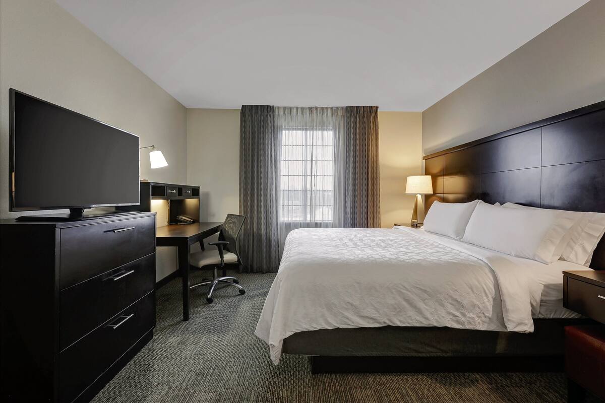 A hotel room with a bed, a desk with a chair, a television, and a lamp.