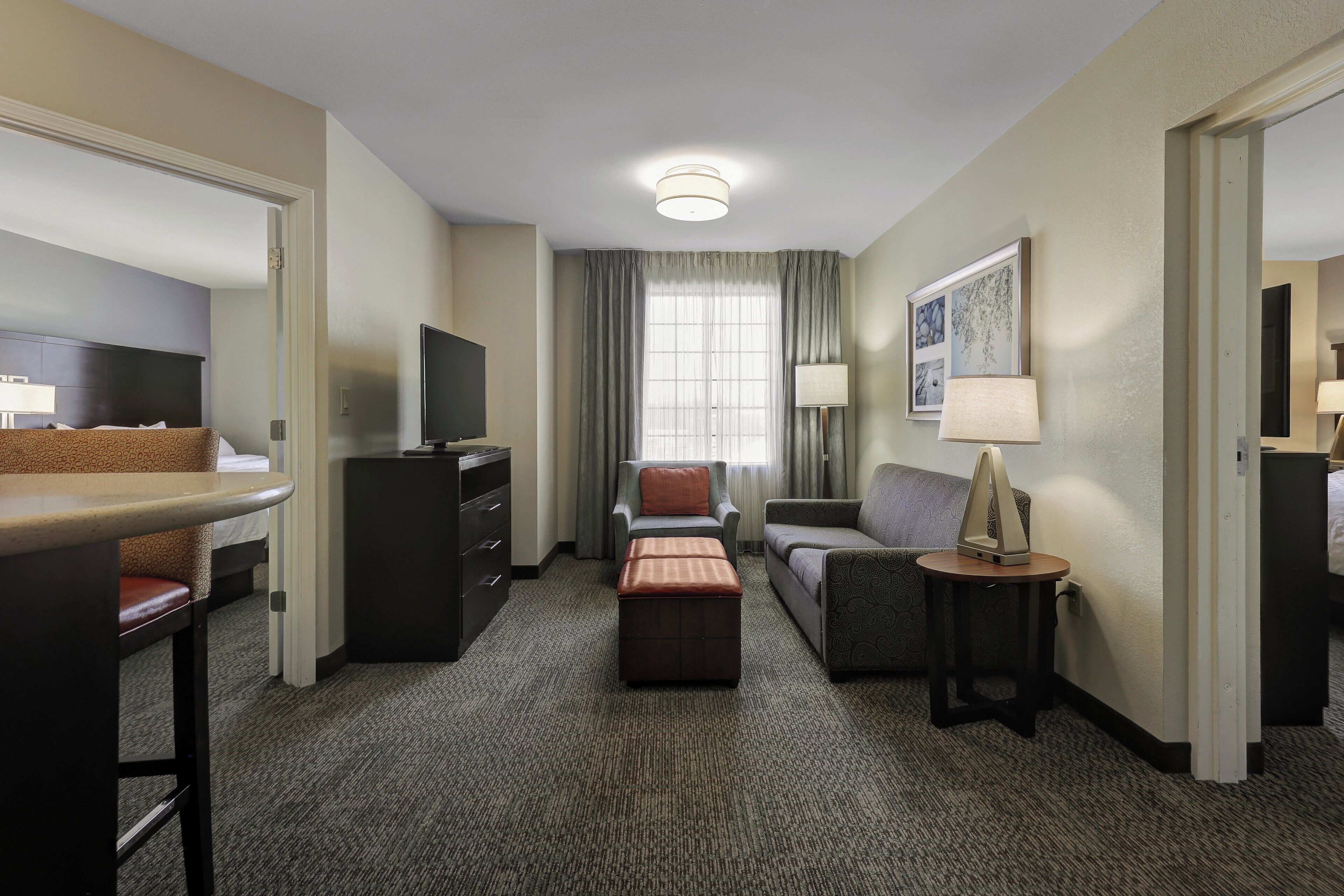 Een hotelkamer met een bed, bureau, televisie, sofa, stoel, een klein tafeltje met lamp en een vloerbedekking.