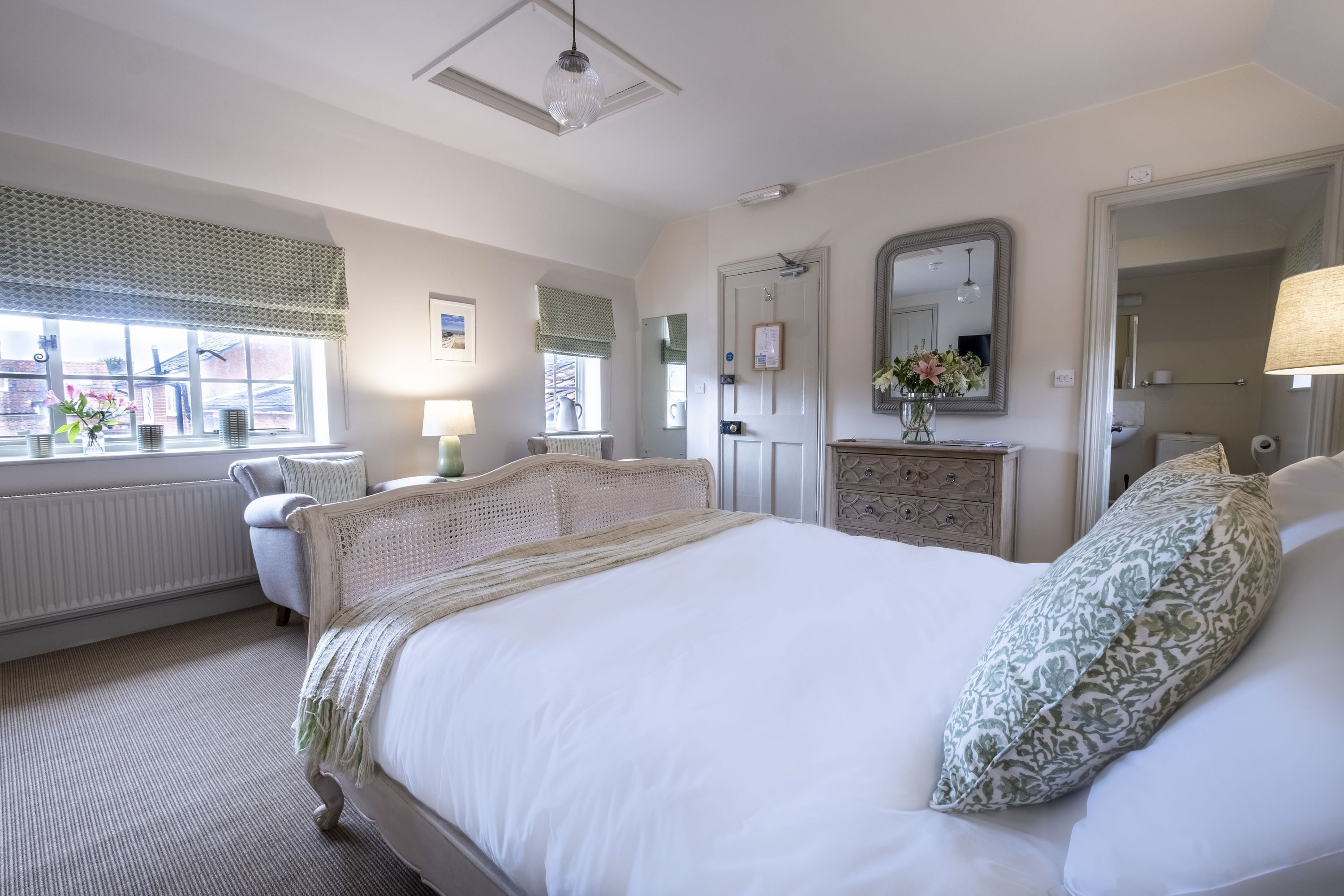 Een slaapkamer met een groot bed, een kaptafel, een spiegel en een raam met jaloezieën.