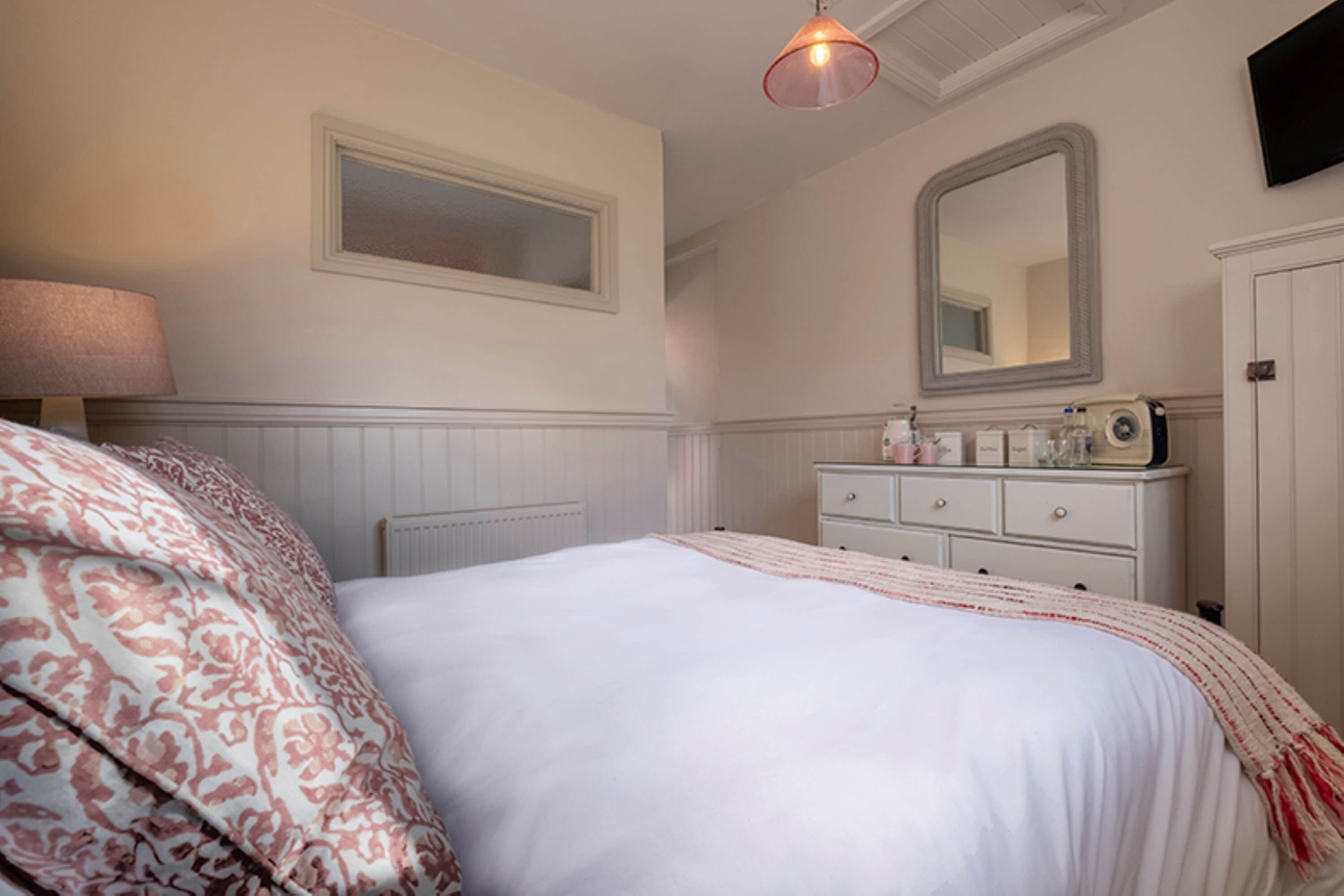 A bedroom with a bed, a dresser, a mirror, a lamp, and a radiator.
