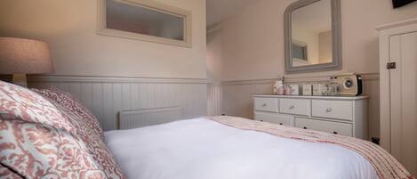 A bedroom with a bed, a dresser, a mirror, a lamp, and a radiator.