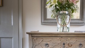 A wooden dresser with ornate carvings and multiple drawers, topped with a clear vase containing flowers. - The Ship at Dunwich (Saxmundham)