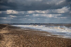 A beach with waves crashing onto the shore under a cloudy sky.