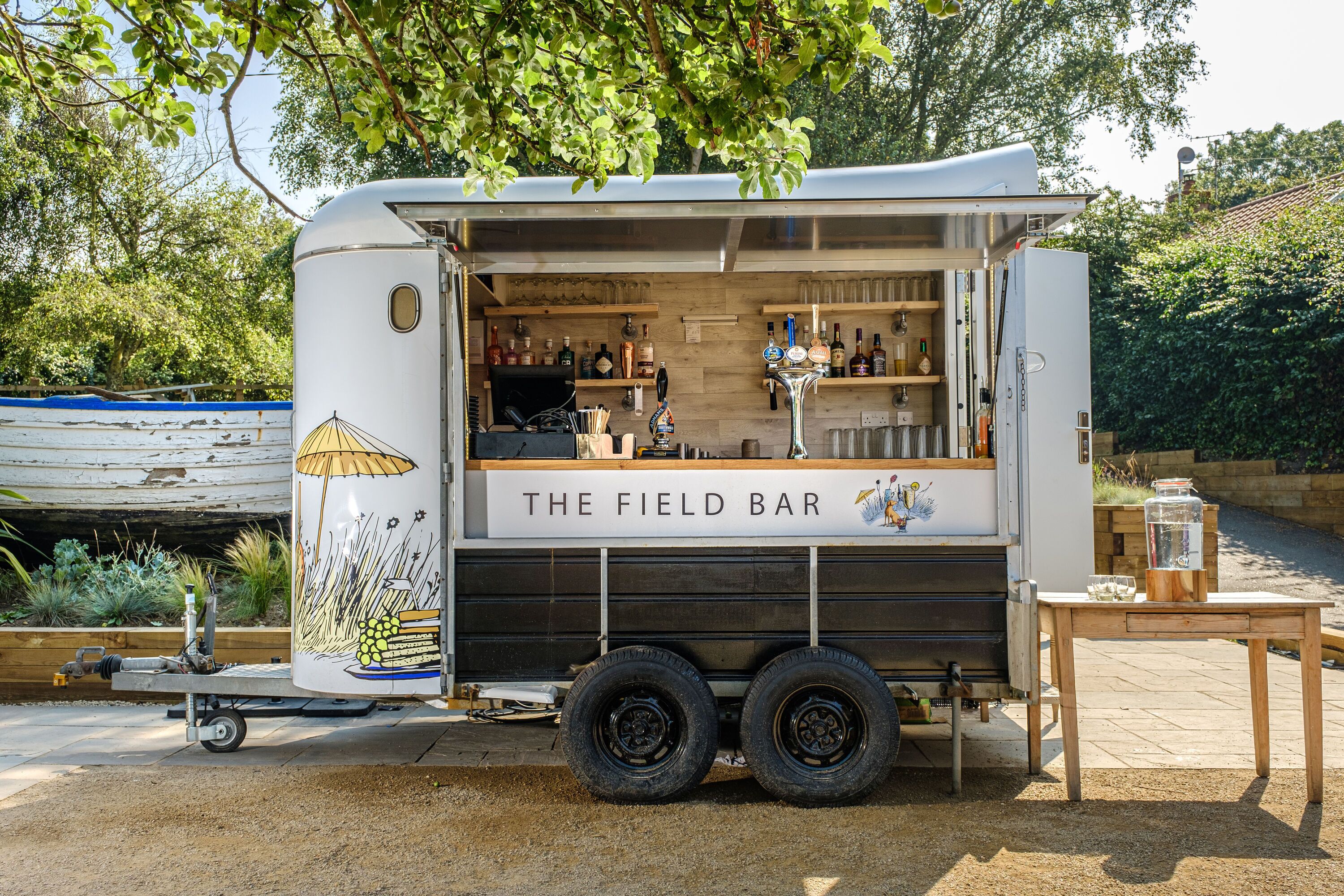 A mobile bar named "The Field Bar" with a wooden interior and a small outdoor seating area.