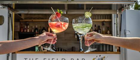 Two people holding drinks in front of a food truck labeled "THE FIELD BAR".