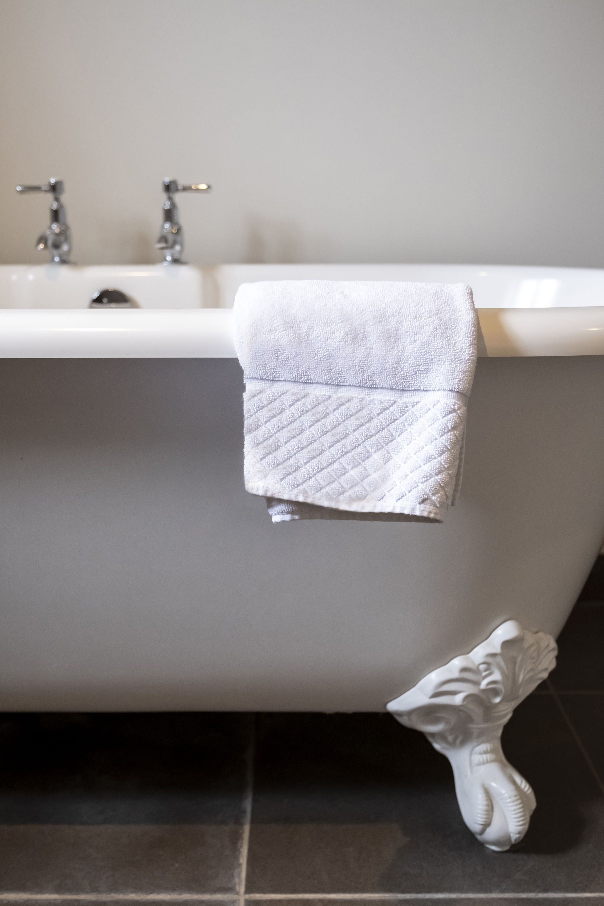 Ein Badezimmer mit einer weißen Badewanne, zwei Wasserhähnen und einem weißen Handtuch, das an der Seite hängt.
