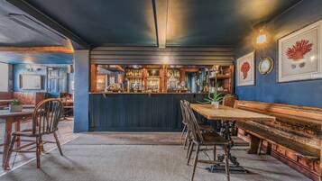 A bar area with wooden furniture, a counter with bottles, and framed artwork on the wall.