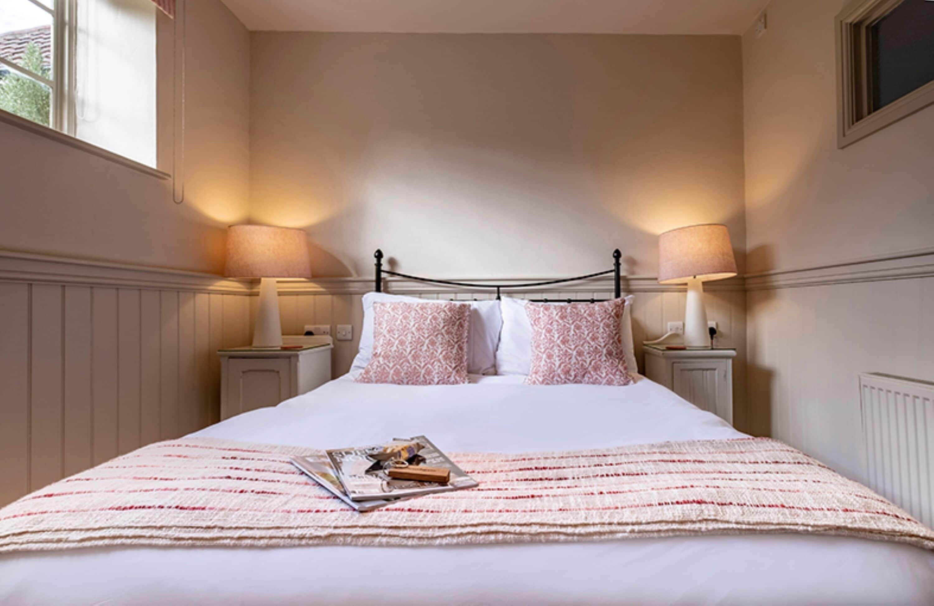 A neatly made bed with a white comforter and a striped blanket, two bedside lamps, and a window with a view of greenery outside.