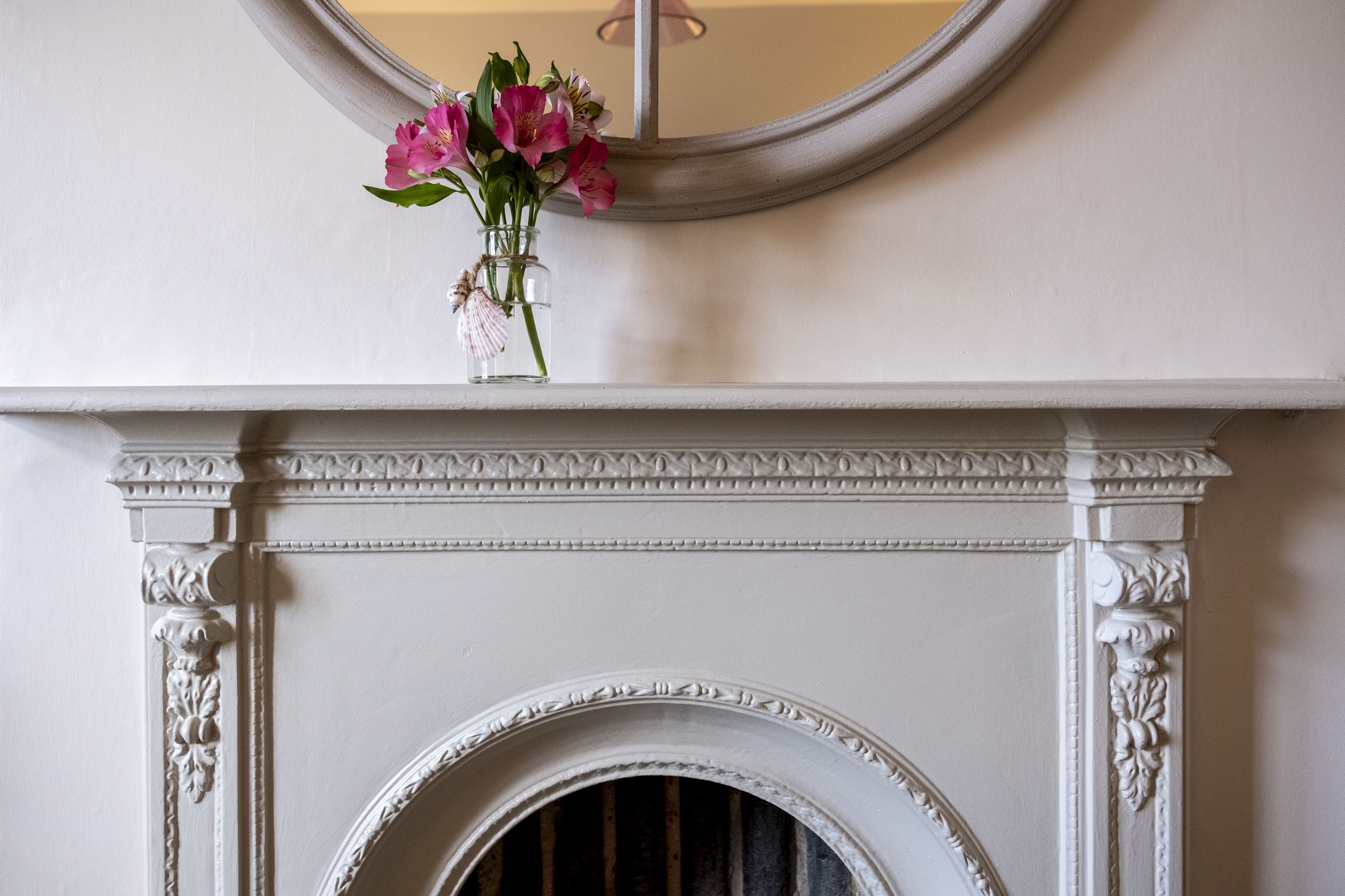 Una chimenea blanca con un arco decorativo y un jarrón con flores rosas sobre la repisa.