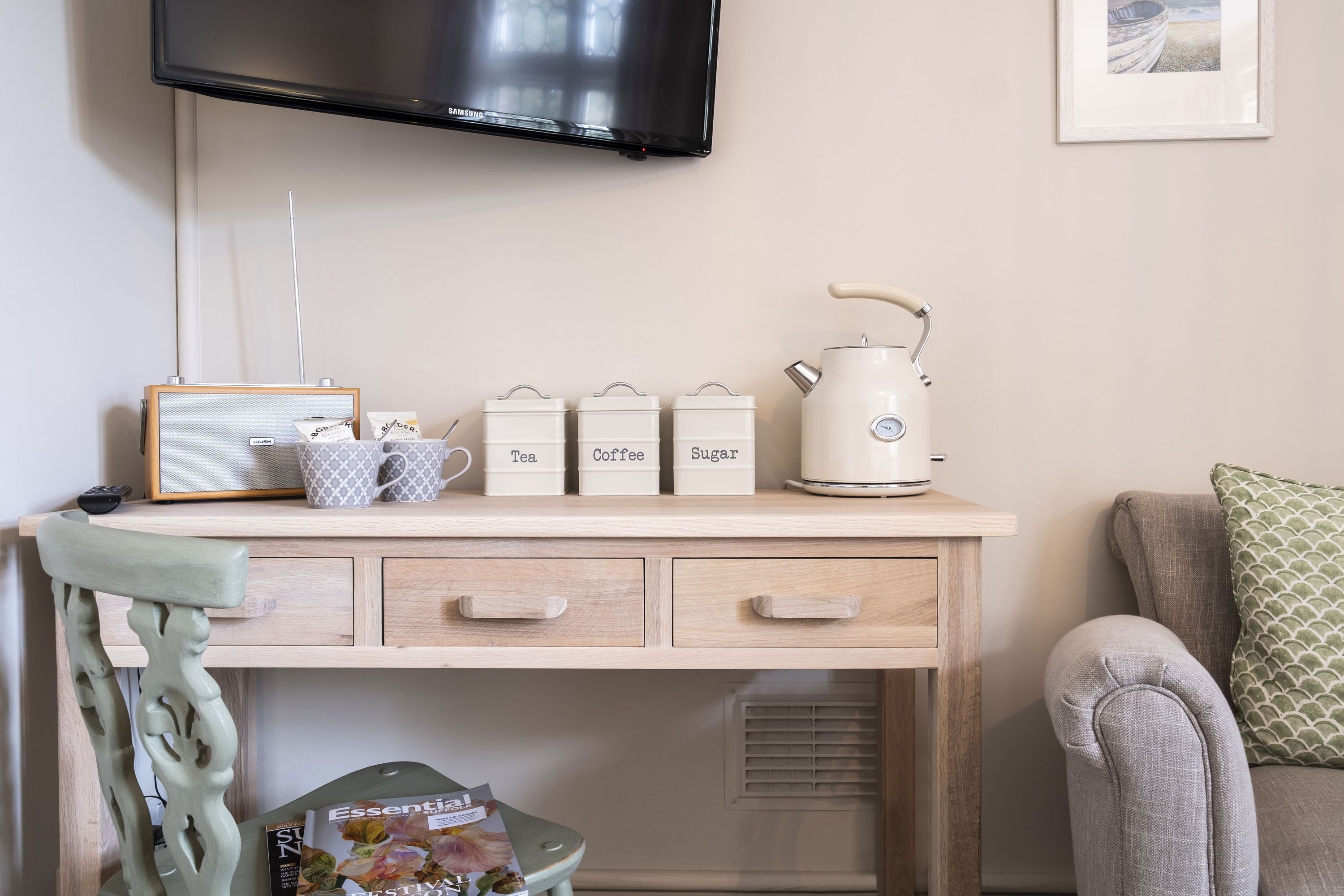 A wooden desk with a coffee maker, tea and coffee containers, and a framed picture on the wall.