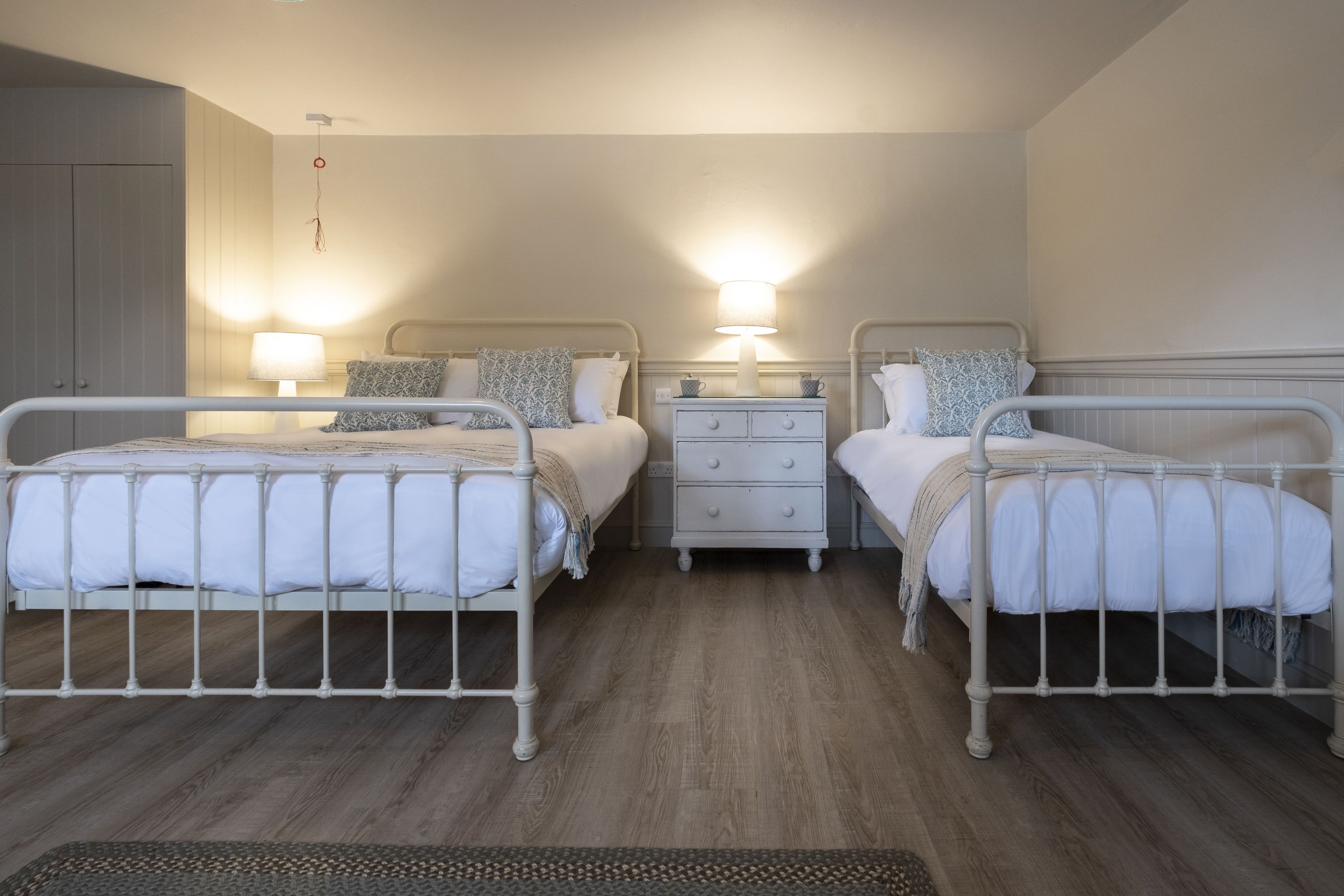 A bedroom with two beds, a nightstand, and a wardrobe.
